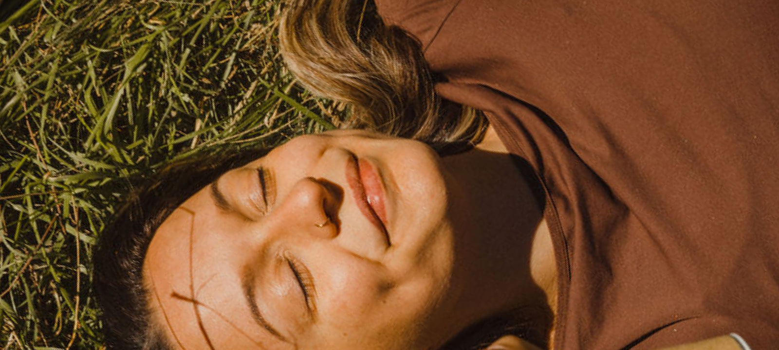Smiling woman laying on a field with the sun shining on her face